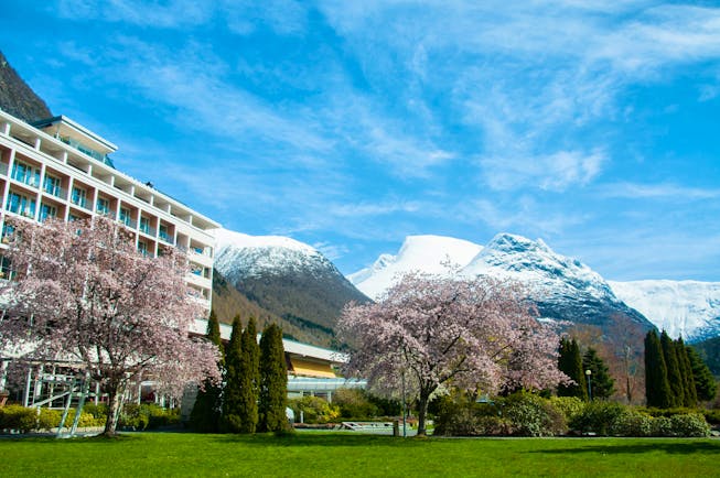 Hotel Alexandra Loen modern hotel with balconies and blossom on trees with snow on mountain tops behind