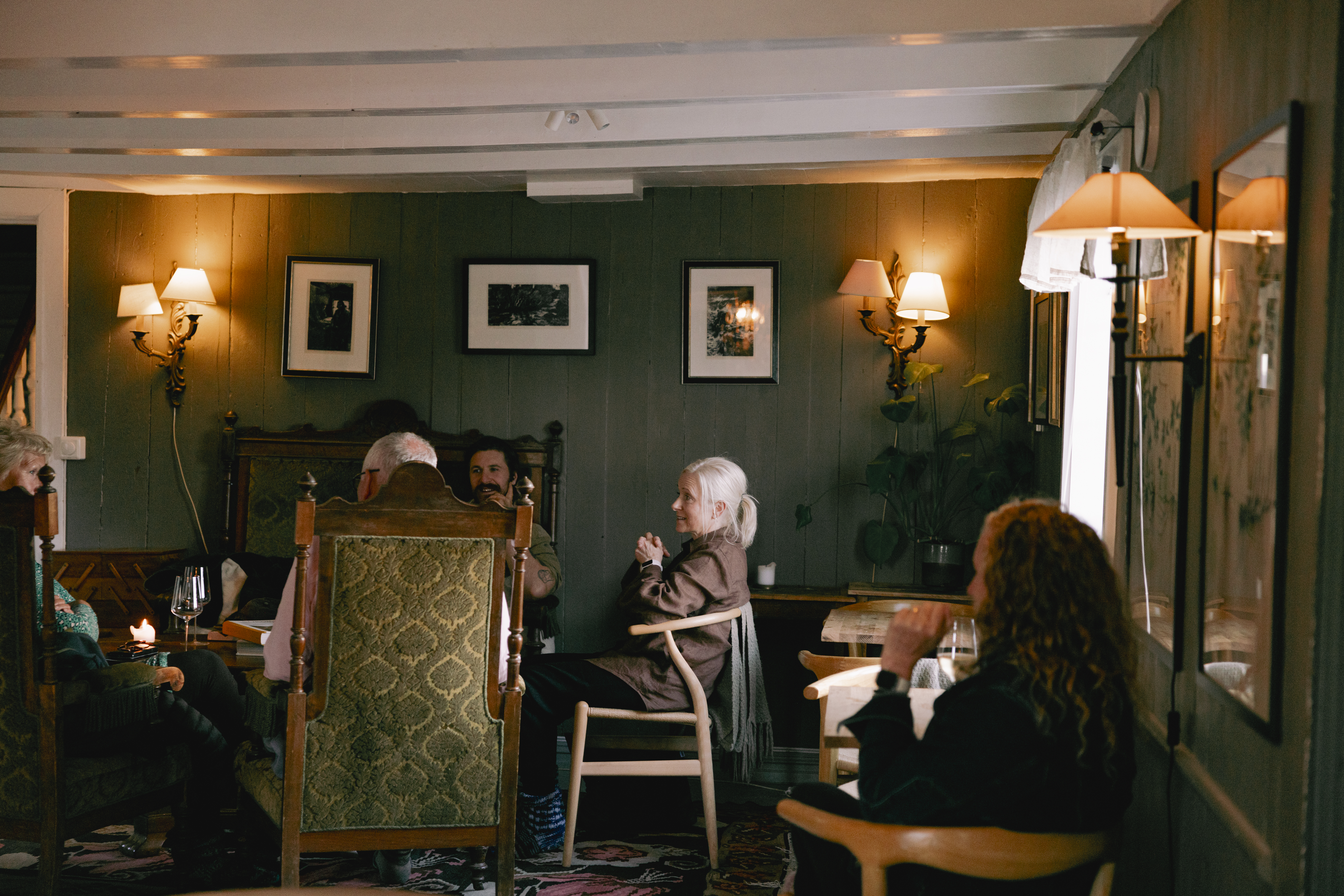 Kvitnes Gard lounge, showing a group gathered around a table on mismatched armchairs, with low beamed white ceiling and dark green walls