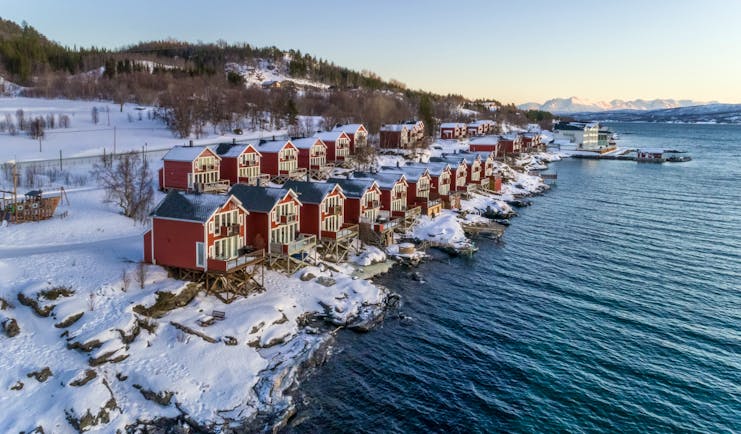 Red huts and cabins in snow on side of water