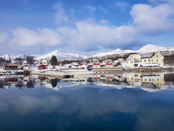 Senja Fjordhotell view of hotel buildings white and red with snowy mountains behind