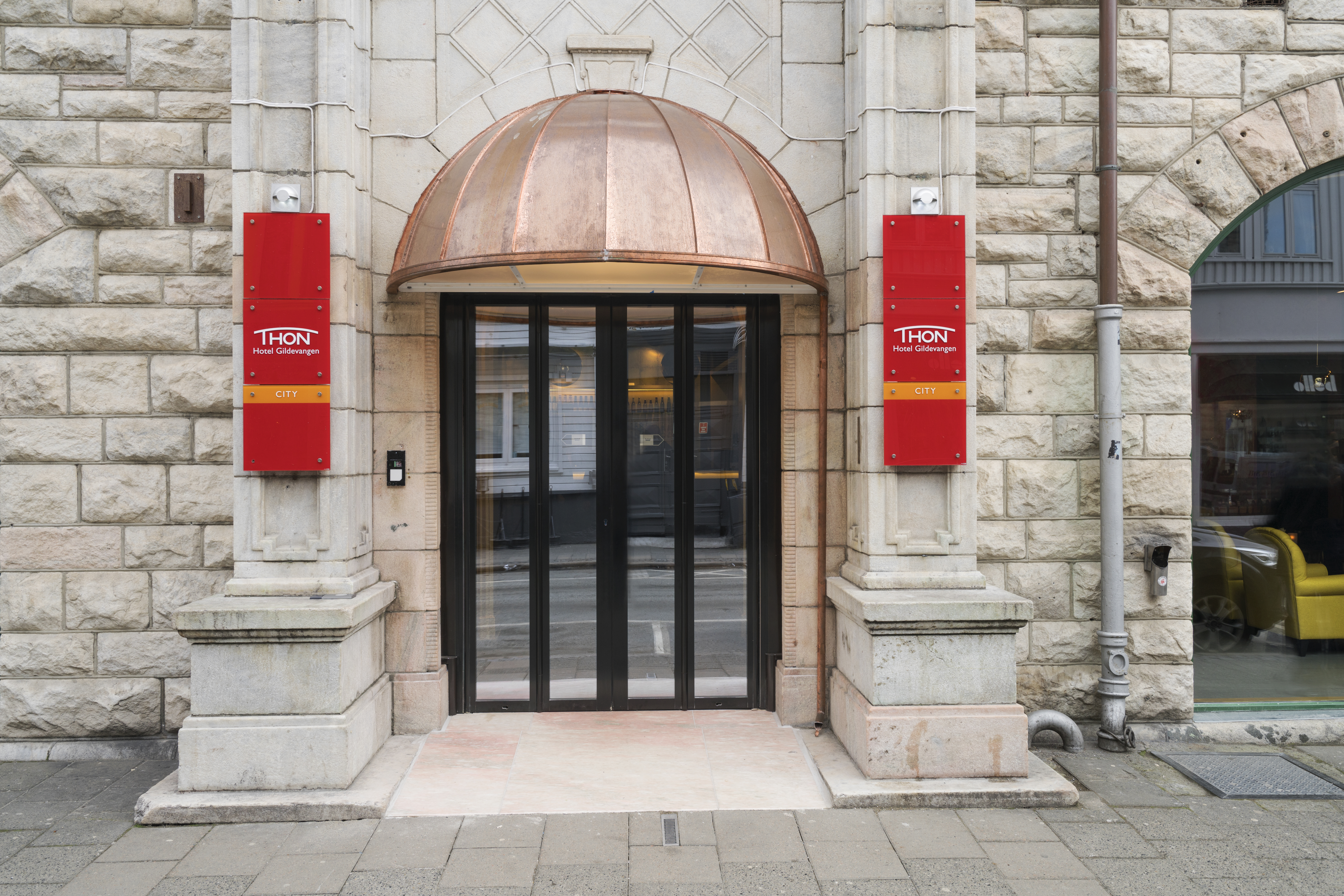 Thon Hotel Nidaros glass and wooden door with red banners either side of entrance