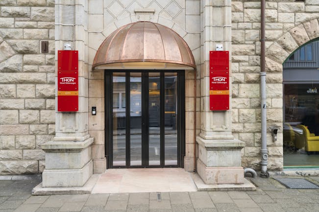 Thon Hotel Nidaros glass and wooden door with red banners either side of entrance