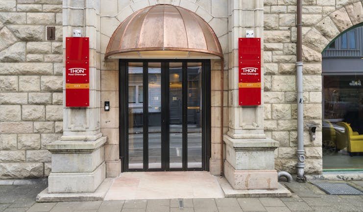Thon Hotel Nidaros glass and wooden door with red banners either side of entrance