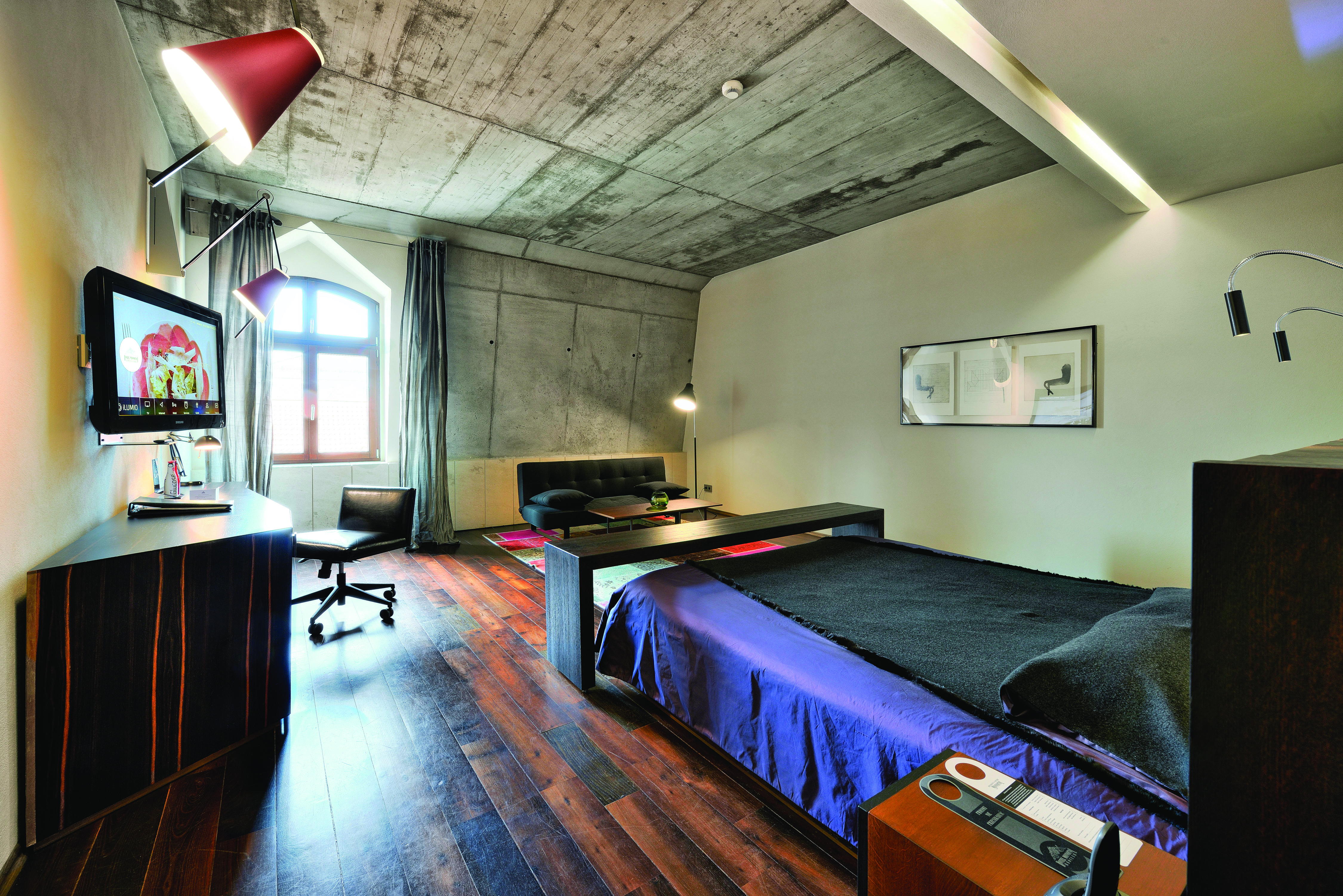 Hotel Monopol Wroclaw deluxe room with stone walls, a black and purple bed, wooden floors and an arched window