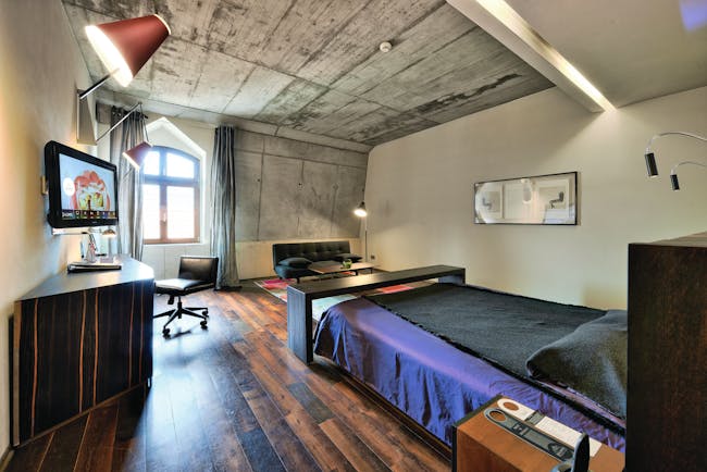Hotel Monopol Wroclaw deluxe room with stone walls, a black and purple bed, wooden floors and an arched window
