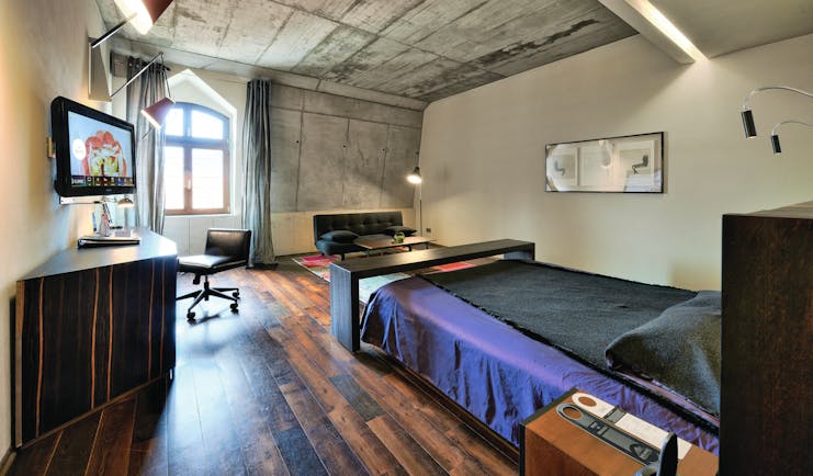 Hotel Monopol Wroclaw deluxe room with stone walls, a black and purple bed, wooden floors and an arched window
