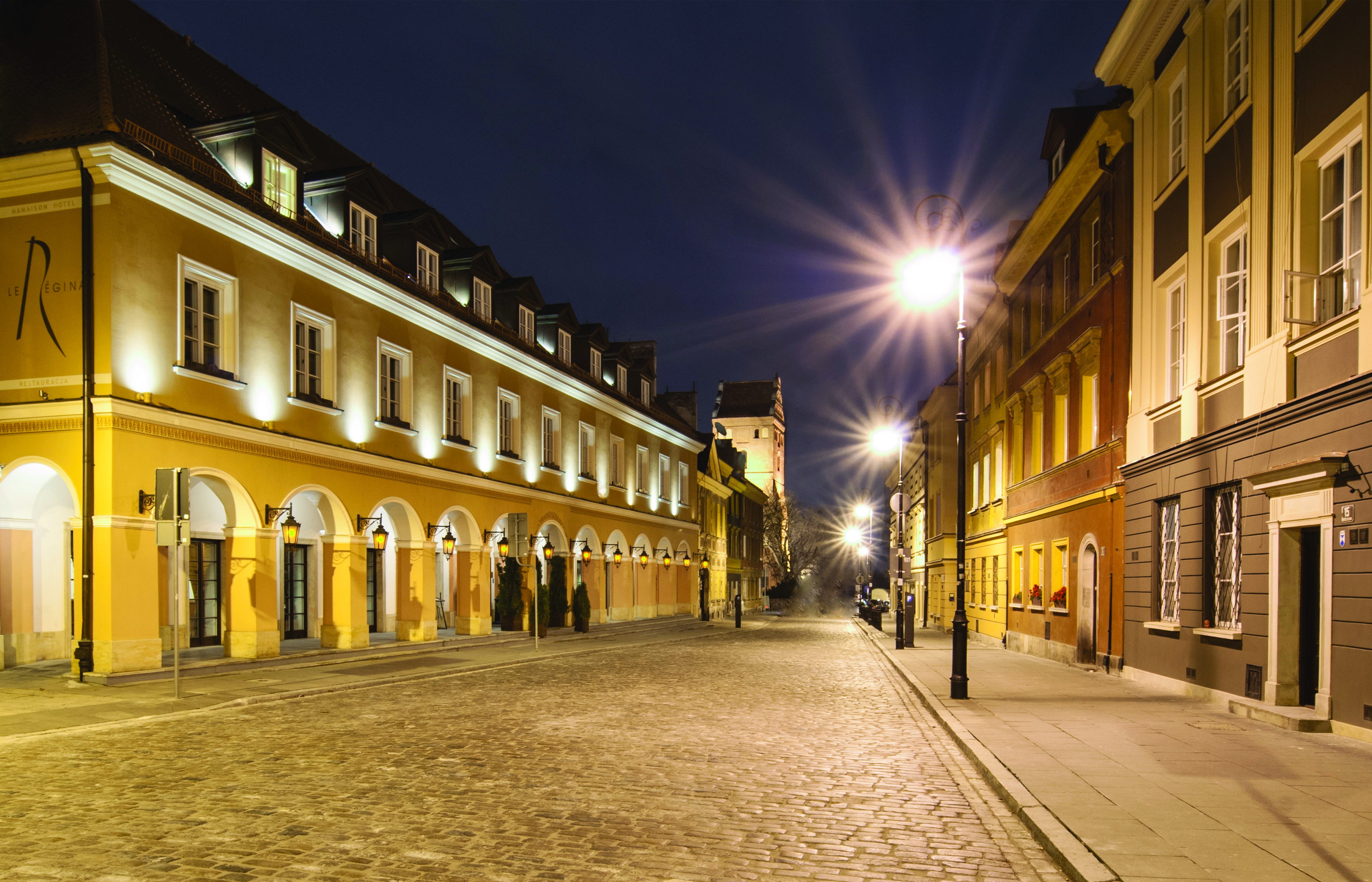 Mamaison Le Regina Warsaw exterior yellow building with archways and lamps on a cobbled street