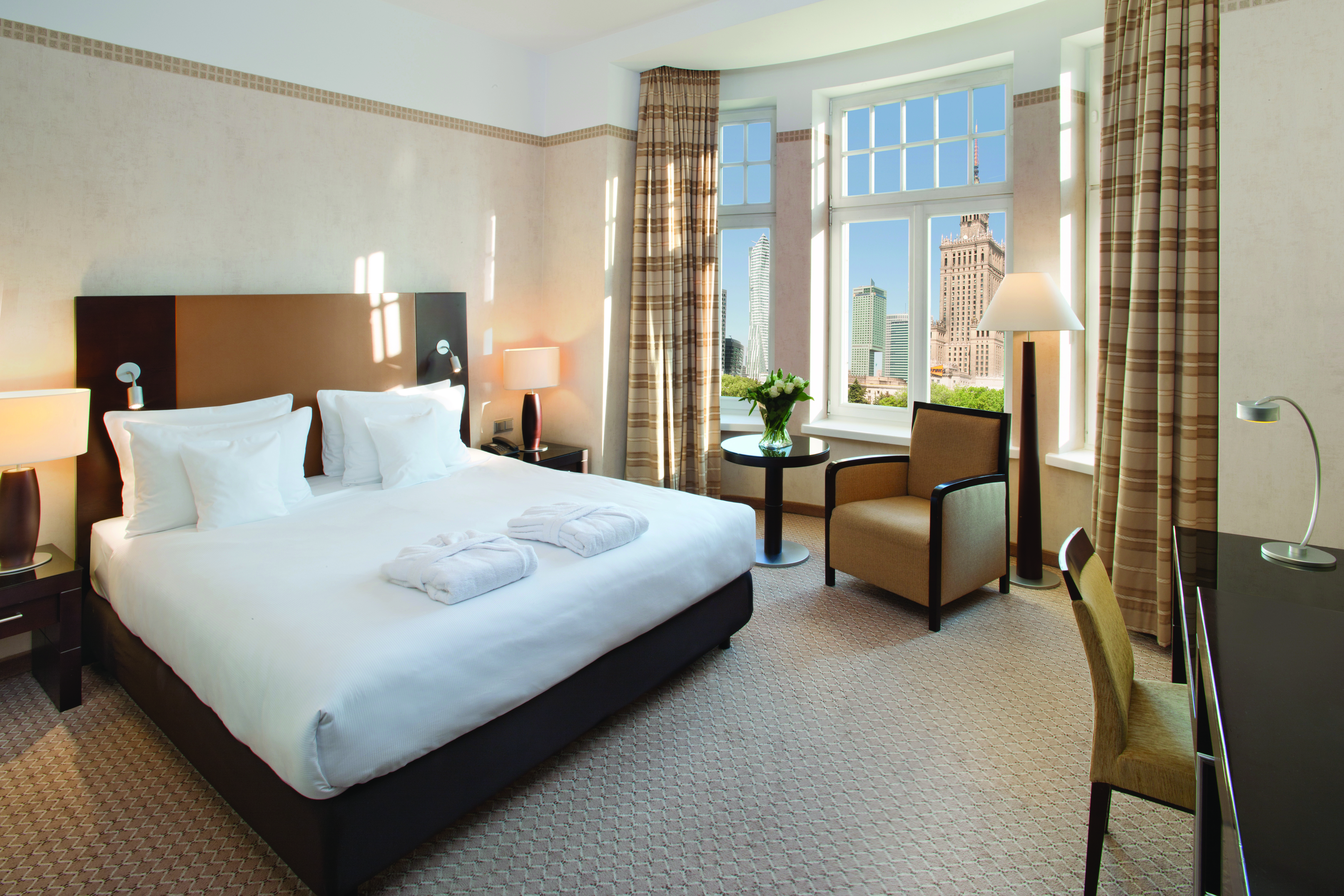 Polonia Palace Hotel deluxe rom with large windows looking over the city, a double bed, a desk and brown and beige colour scheme 