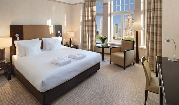 Polonia Palace Hotel deluxe rom with large windows looking over the city, a double bed, a desk and brown and beige colour scheme