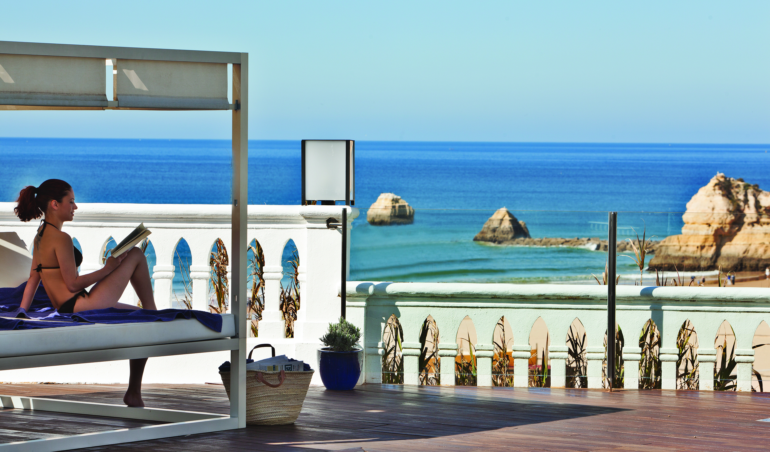 Woman sitting reading a book by the pool at Bela Vista Hotel & Spa, looking onto the blue sea 