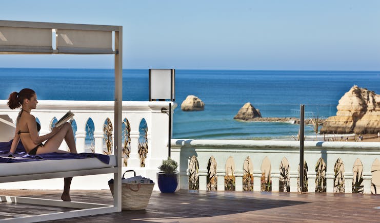 Woman sitting reading a book by the pool at Bela Vista Hotel & Spa, looking onto the blue sea