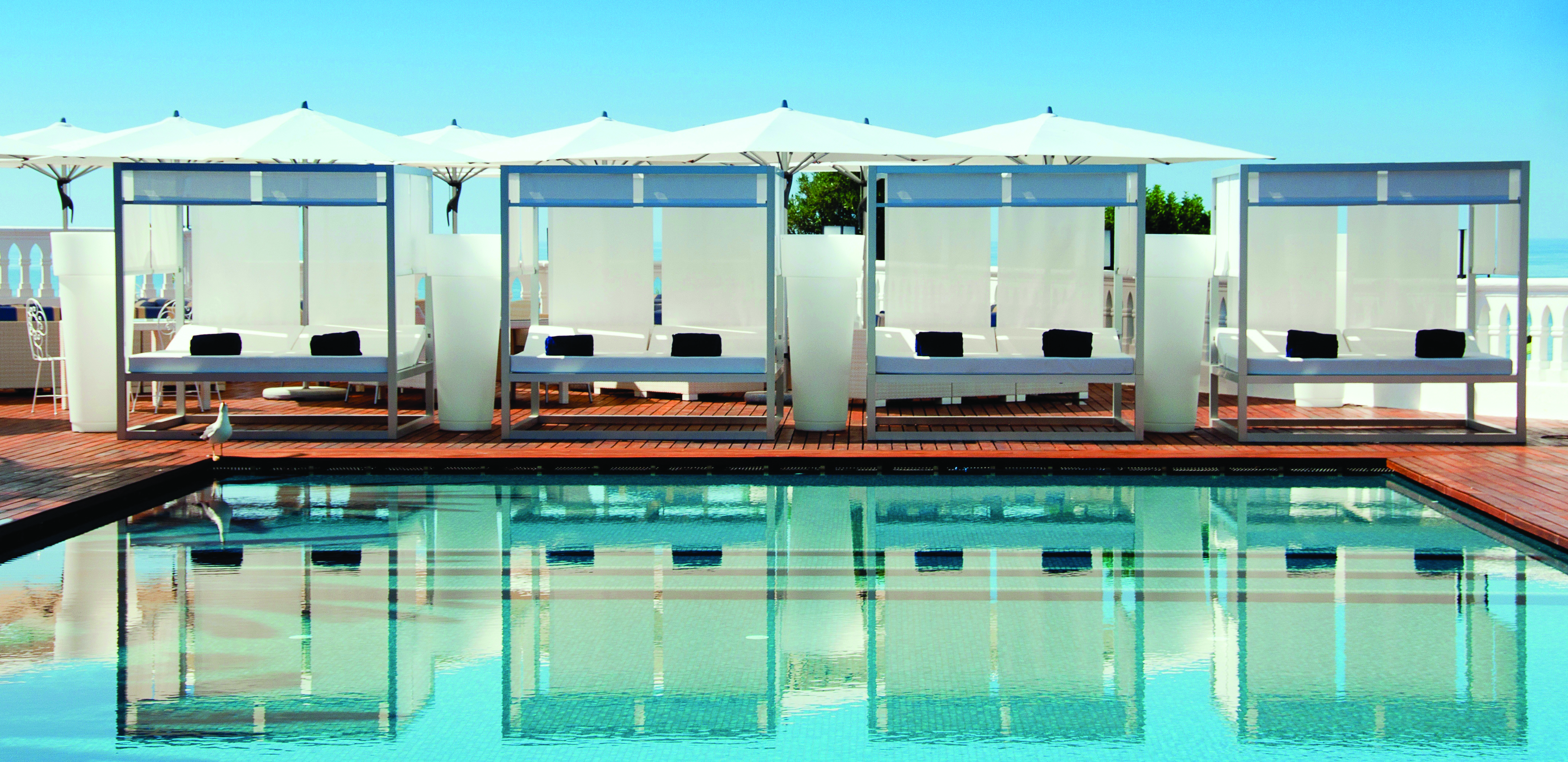 View of the clear blue pool at Bela Vista Hotel & Spa with cabana sunbeds shown reflecting in the water