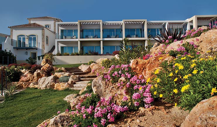 View of the Bela Vista Hotel & Spa from the gardens, displaying green grass and pink and yellow flowers 