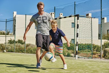 Father and son playing football together on the Martinhal Beach Resort and Hotel grounds