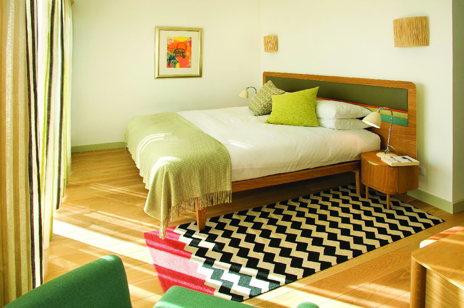 View of the Martinhal Beach Resort and Hotel Ocean house bedroom with a large double bed, wooden floors, a rug and an armchair, decorated in green and white