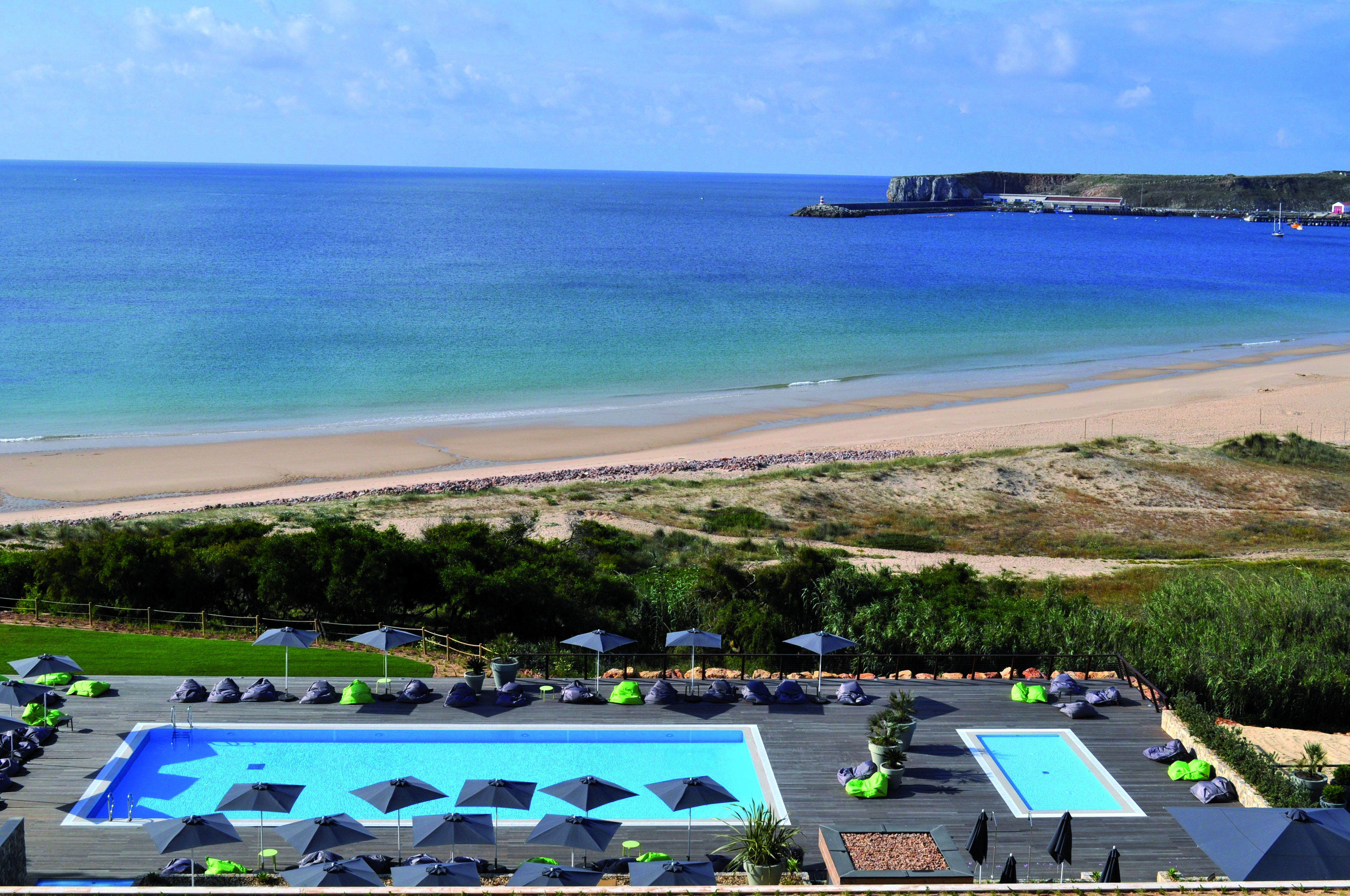 View of the main beach club pool and children's plunge pool on wooden decking overlooking the sandy beach and ocean