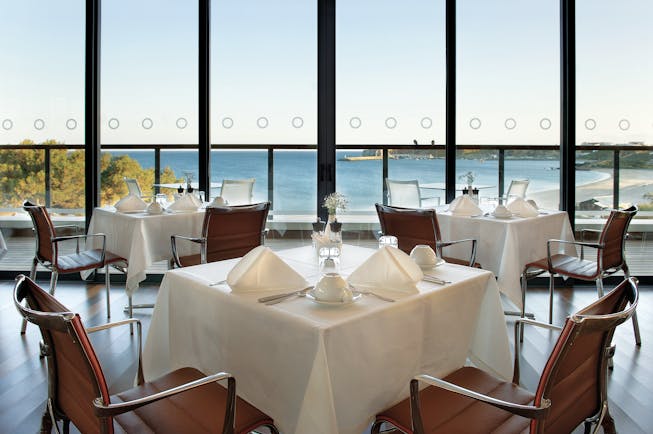 Terrace restaurant at the Martinhal Beach Resort and Hotel, showing dining tables and chairs set out in a room overlooking the sea with big windows