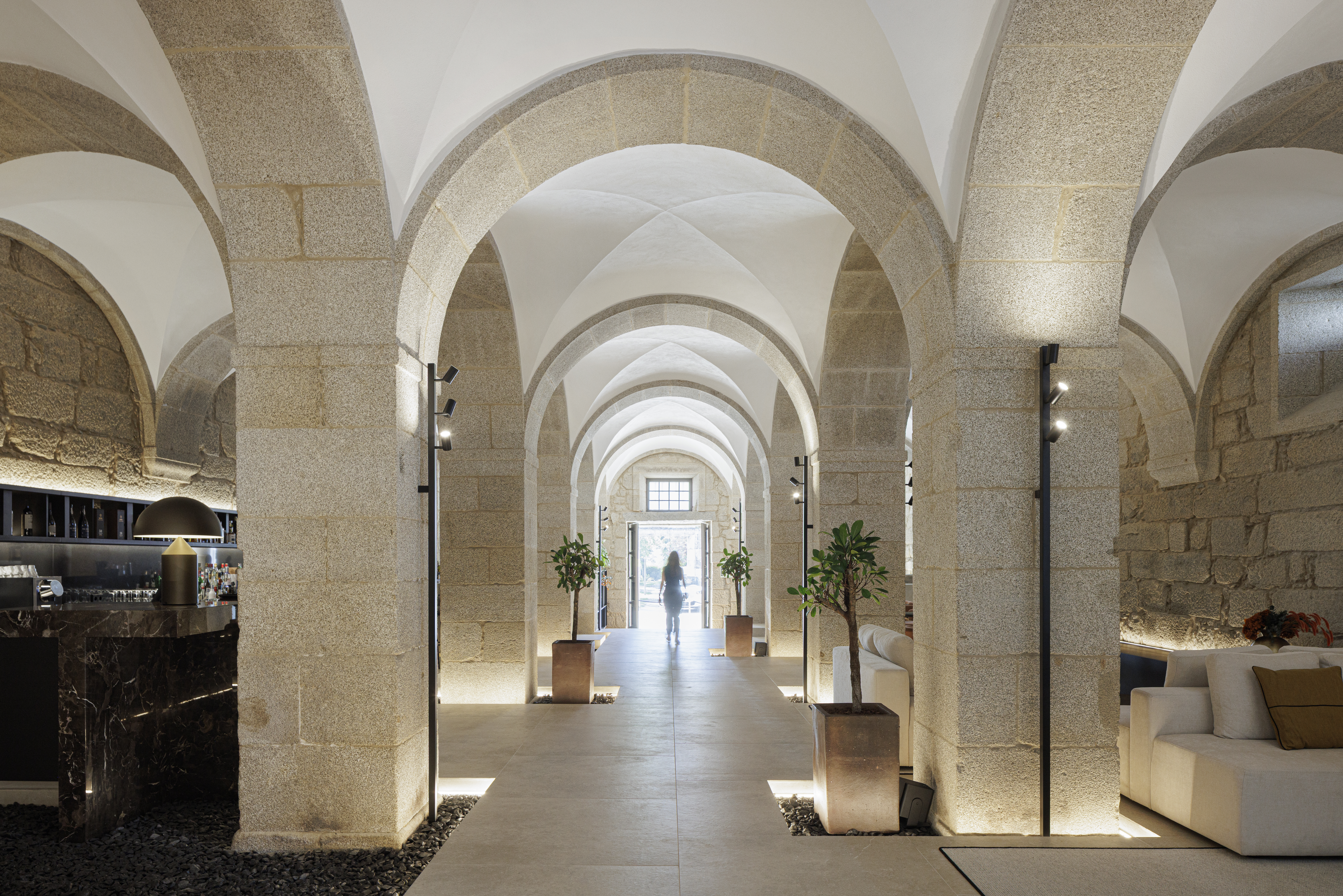 Mosterio de Arouca lobby and bar area, with repeated symmetrical stone arches marking a central walkway, with bar on one side and sofas on the other