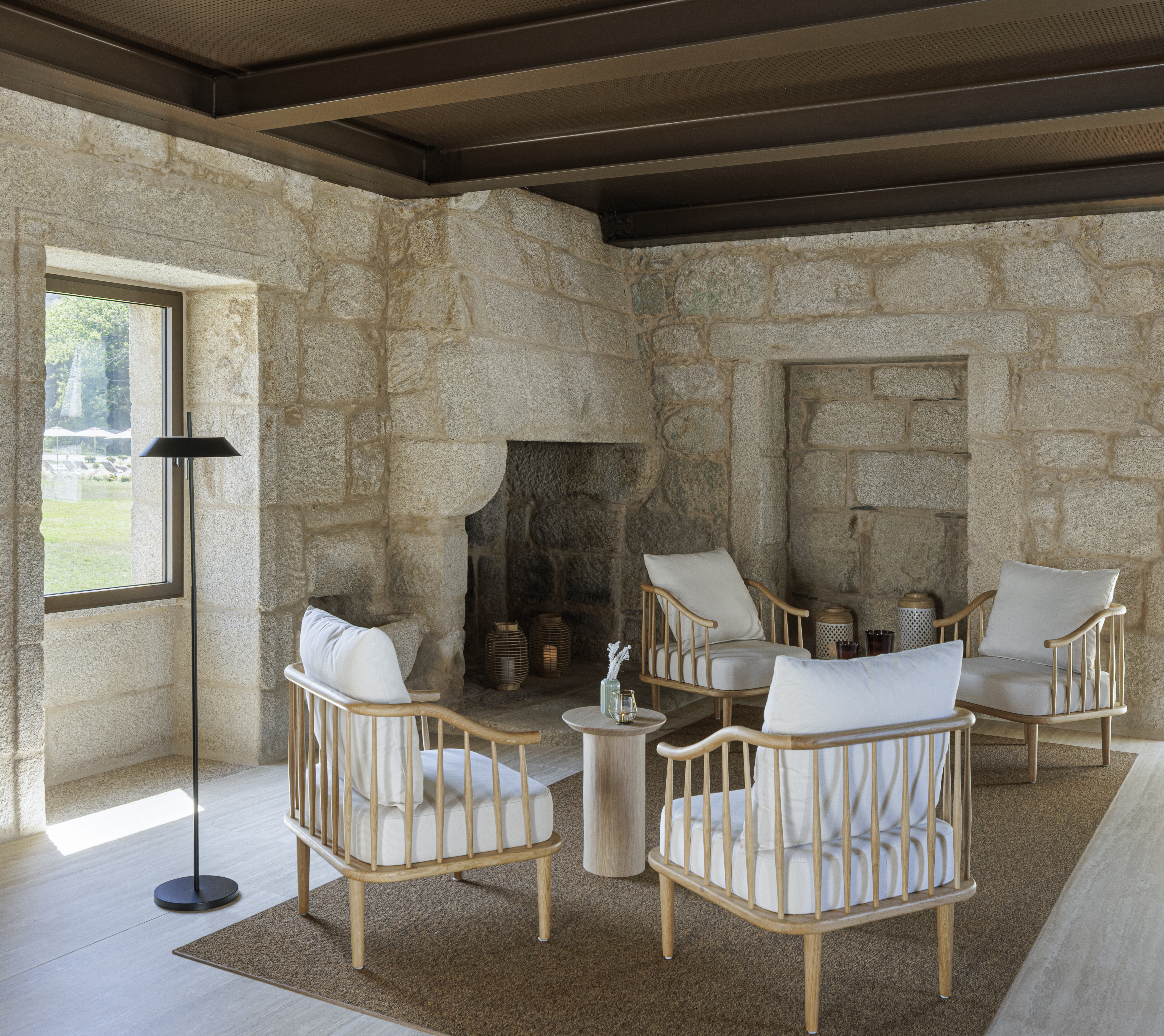 Mosterio de Arouca spa relaxation area, with traditional stone walls, beamed wooden ceiling, fireplace, and white armchairs