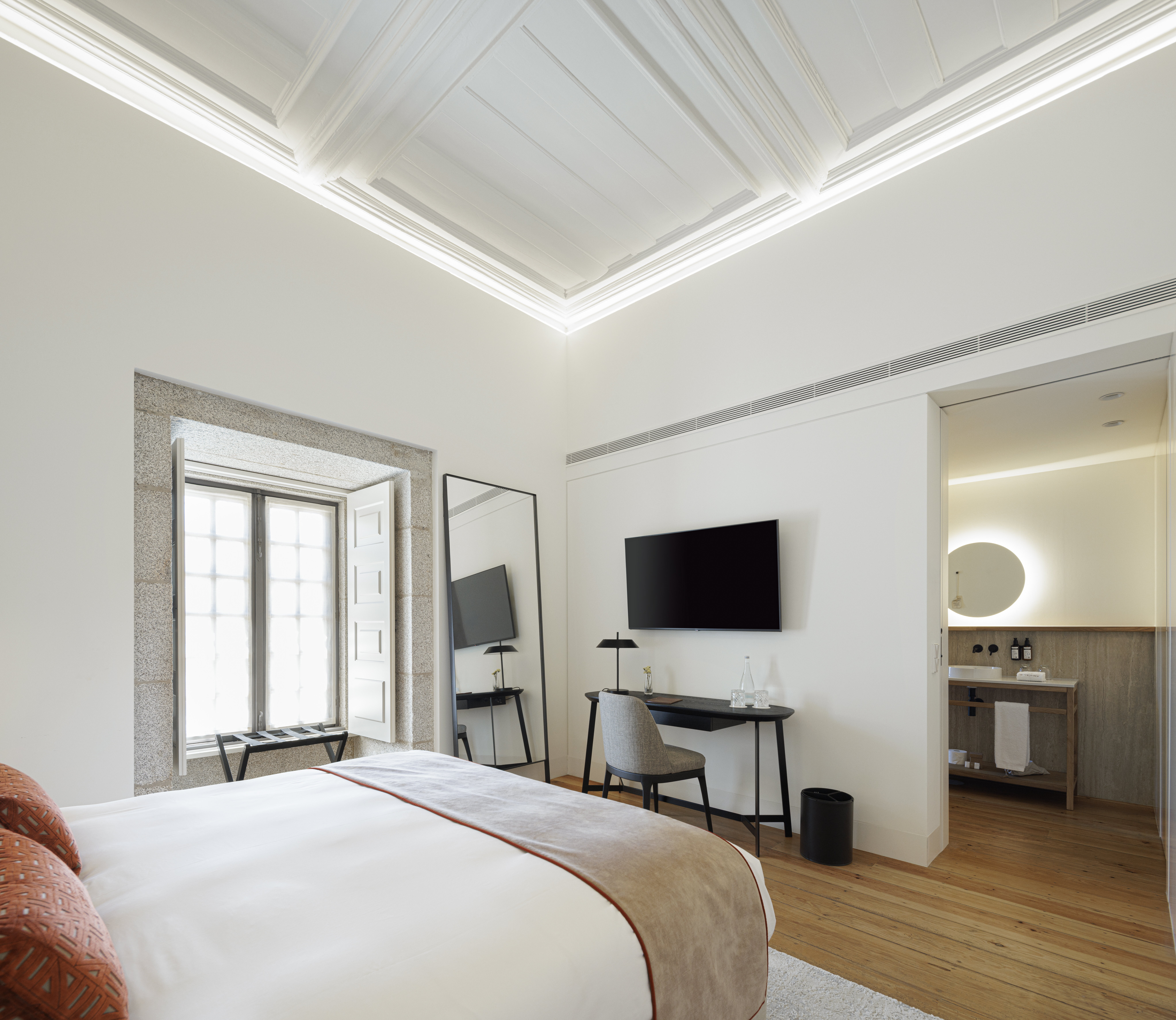 Mosterio de Arouca guest room with high, vaulted, lit ceilings, white walls, neutral colour palette, and stone-framed windows