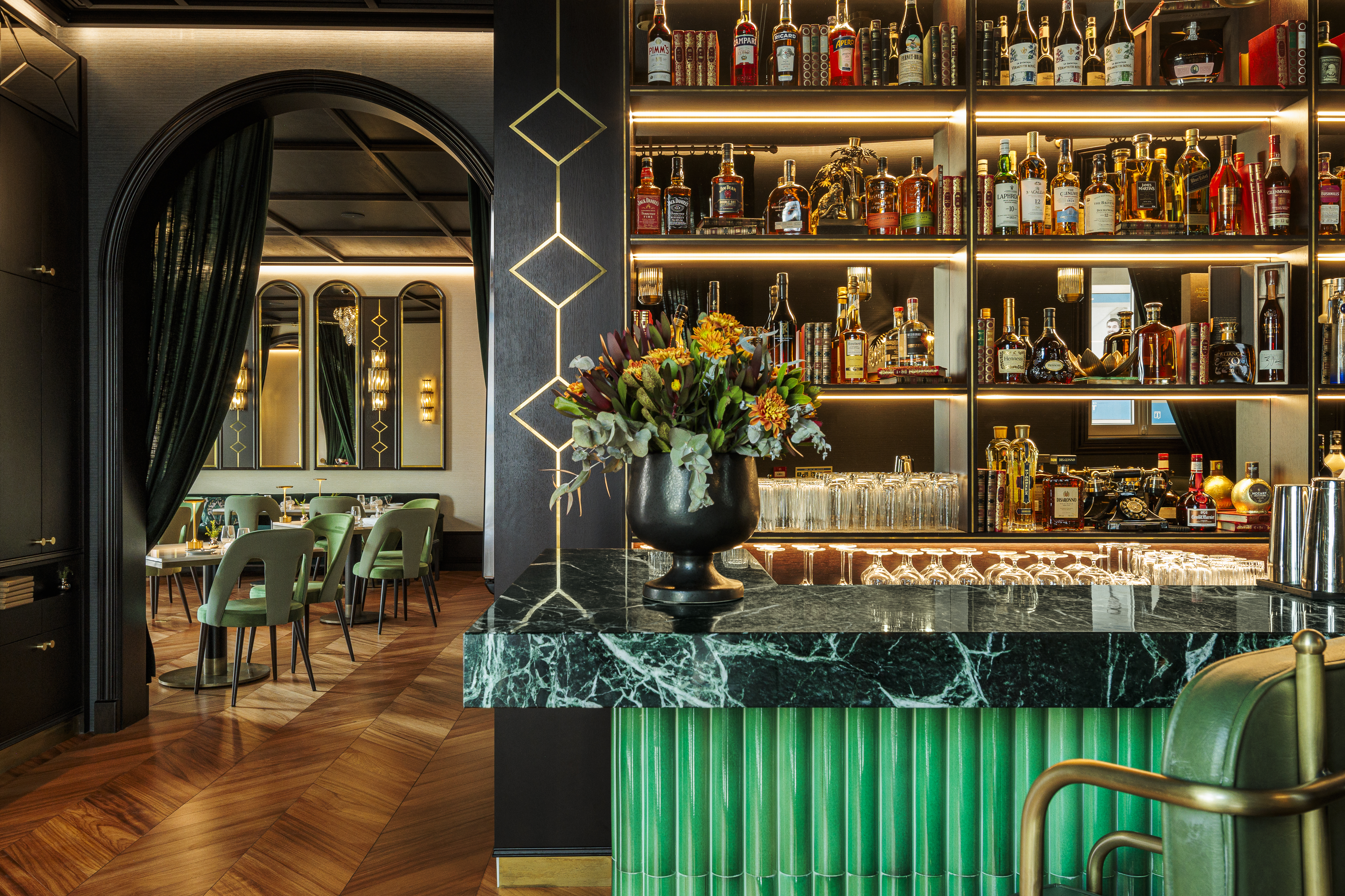 Palacete de Valdemouro sumptuous bar area, with lit shelves of many colourful bottles, green leather and gold bar stools, and, through a curtained archway, the tables and chairs of the restaurant