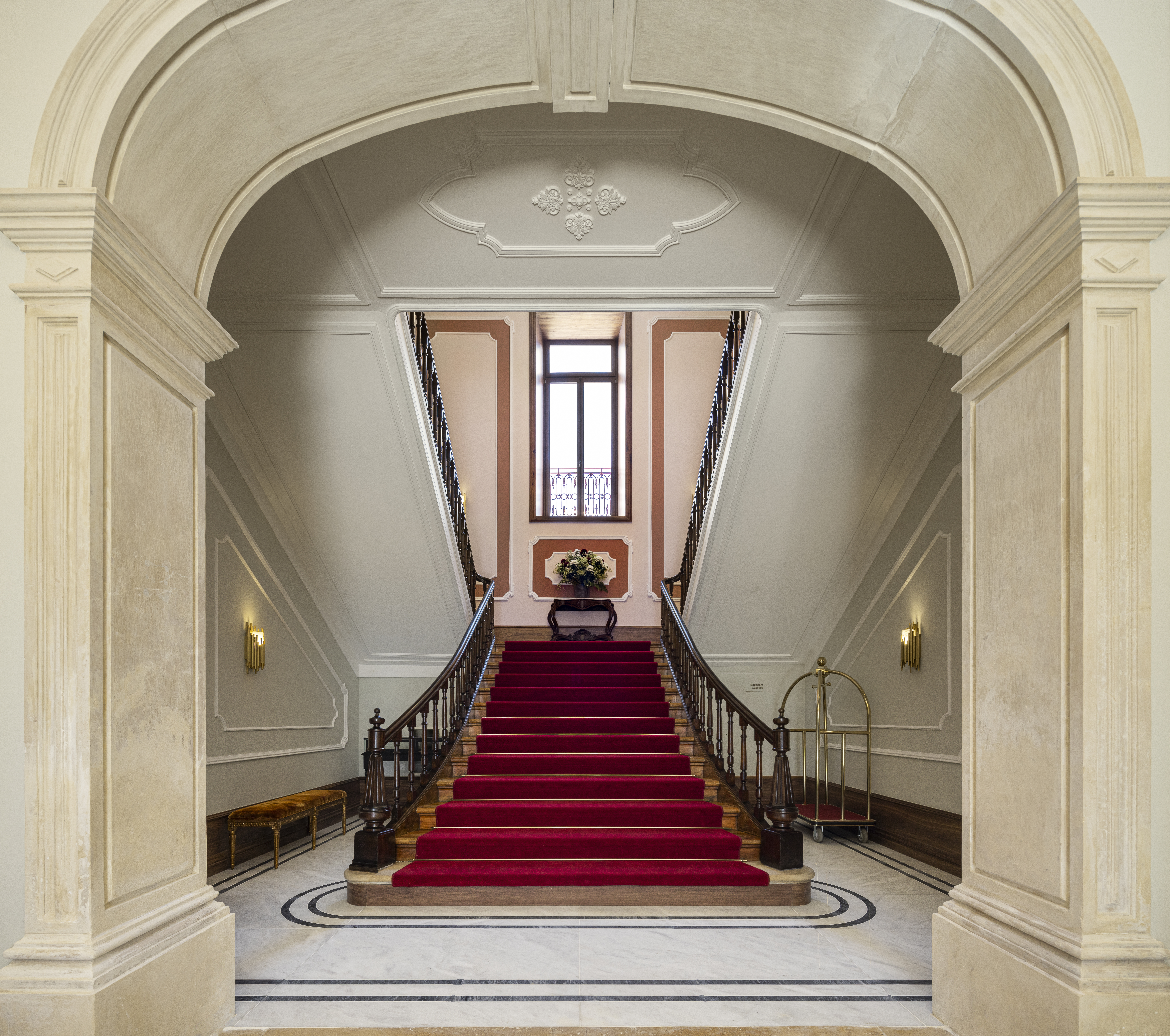 Palacete de Valdemouro grand staircase in the hotel entrance, with red carpet against stone steps, and ornate stone walls and archway