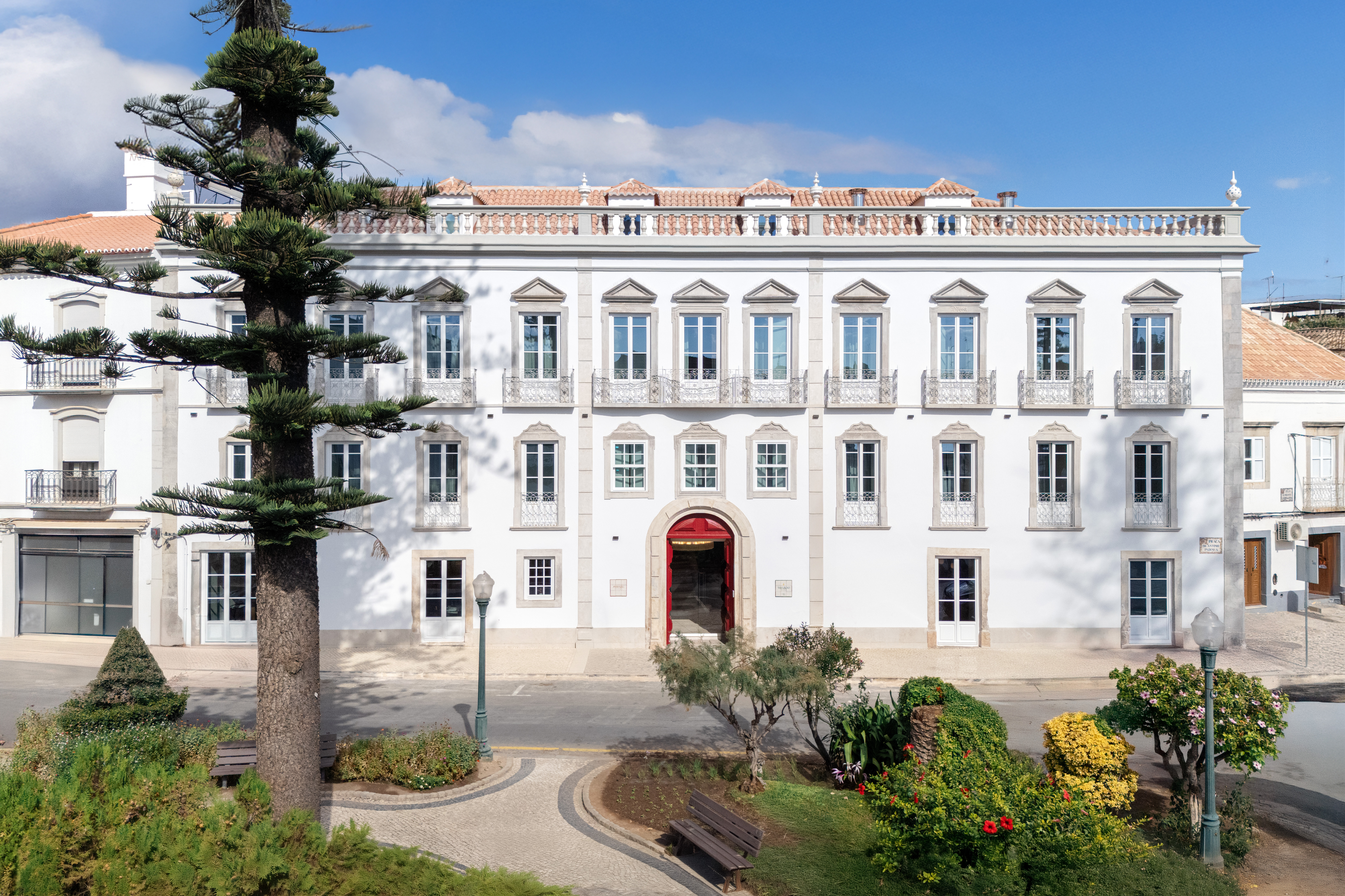 Palacio de Tavira palacial exterior, with many tall windows, red front door, white stone walls, and gardens in the foreground