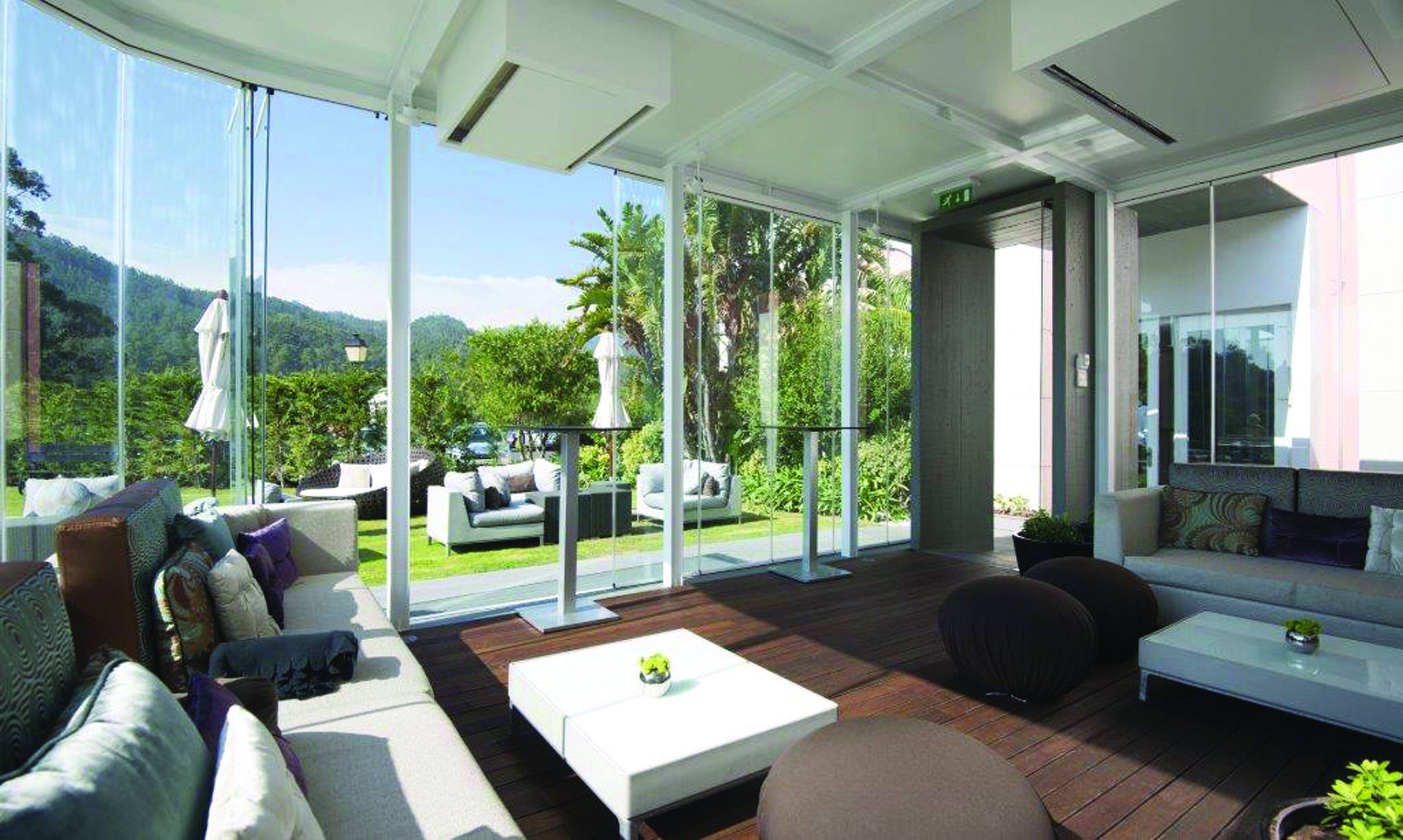 Indoor lounge area with sofas, with bi-folding doors opening onto a terrace with sofas laid out 