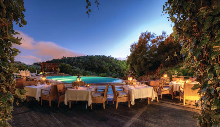 Outdoor dining area of Aqua Restaurant with tables and chairs set up on wooden dekcing looking over the pool 