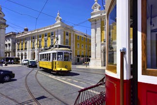 Yellow and white tram in road in front of yellow and white ornate building in Lisbon
