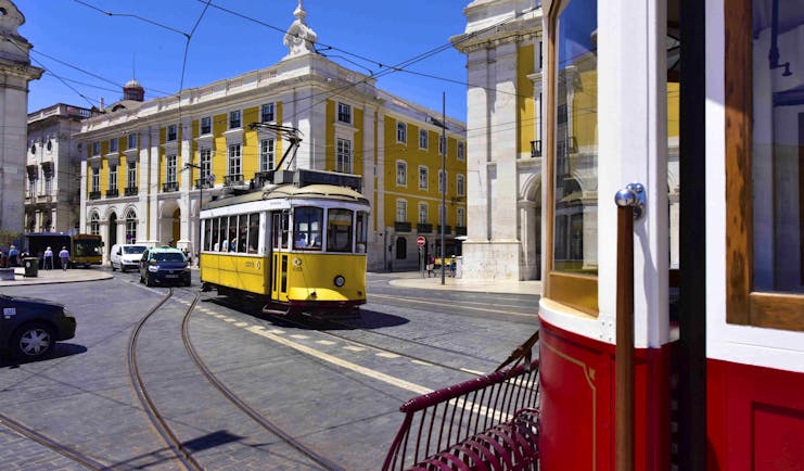 Yellow and white tram in road in front of yellow and white ornate building in Lisbon