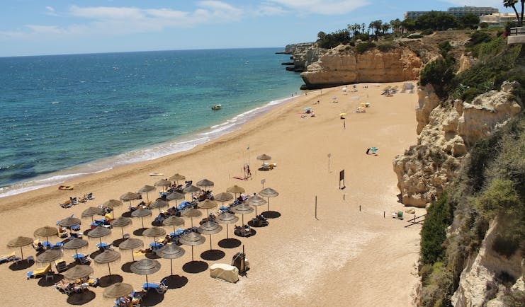 View of a sandy beach from the vilalara thalassa resort with umbrella's set up 