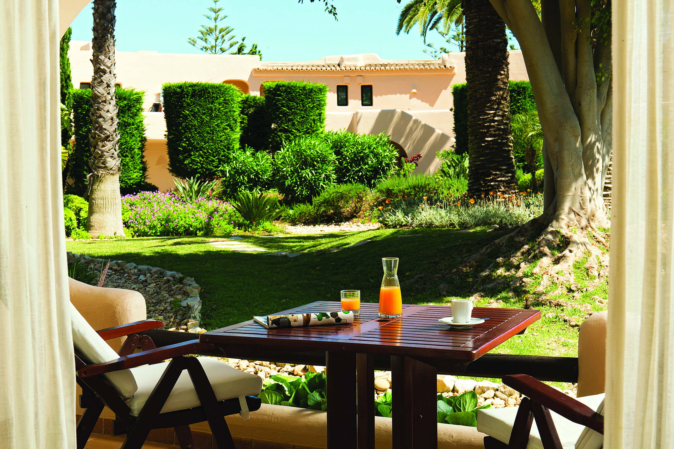 Garden view from a junior suite at the vilalara thalassa resort, showing a wooden table in the garden and neatly trimmed hedges 