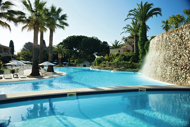 View of the swimming pool at the vilalara thalassa resort with palm trees and white umbrellas around the edge