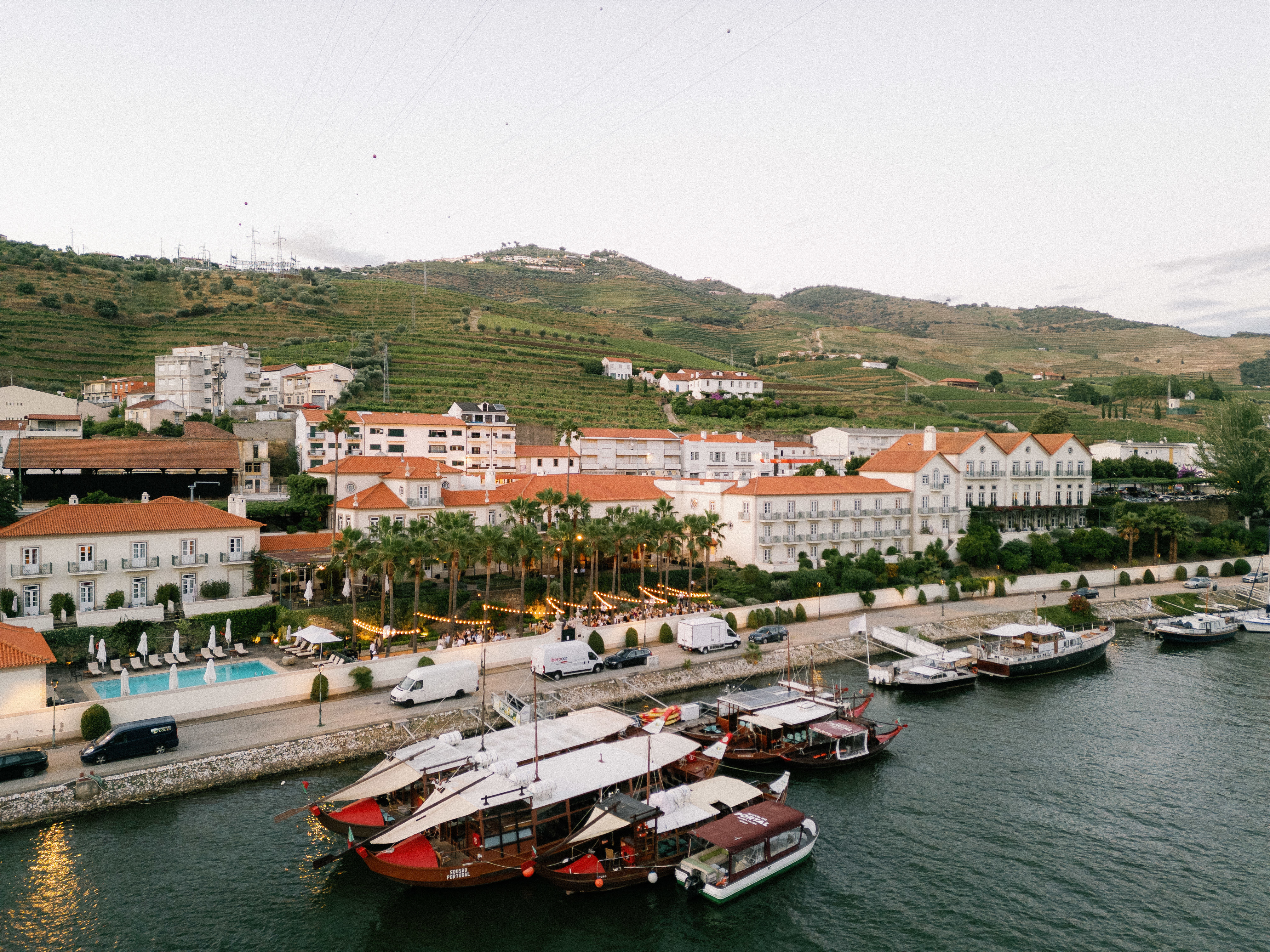 Vintage House Pinhao view of the hotel from above the river, with its white-washed walls and terracotta roofs, and boats in the foreground and hills in the background