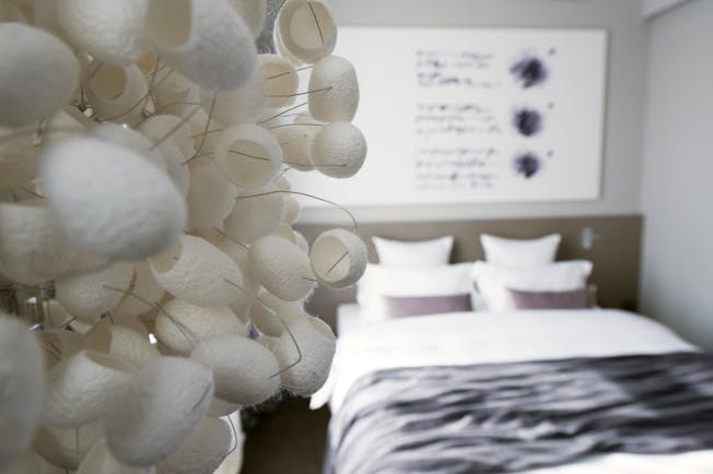 Hotel Cubo guestroom, focus on fake flower installation, double bed, painting, bright modern decor