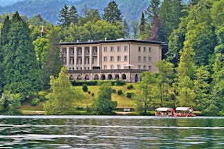 Vila Bled lake view large building with stone archways on a hill above a lake surrounded by trees