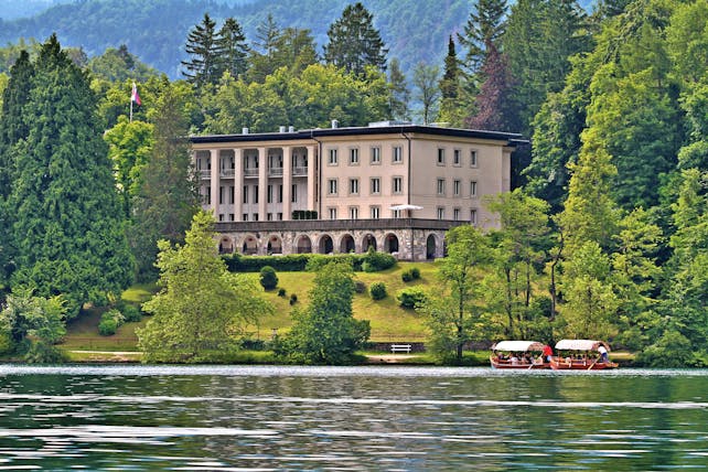 Vila Bled lake view large building with stone archways on a hill above a lake surrounded by trees