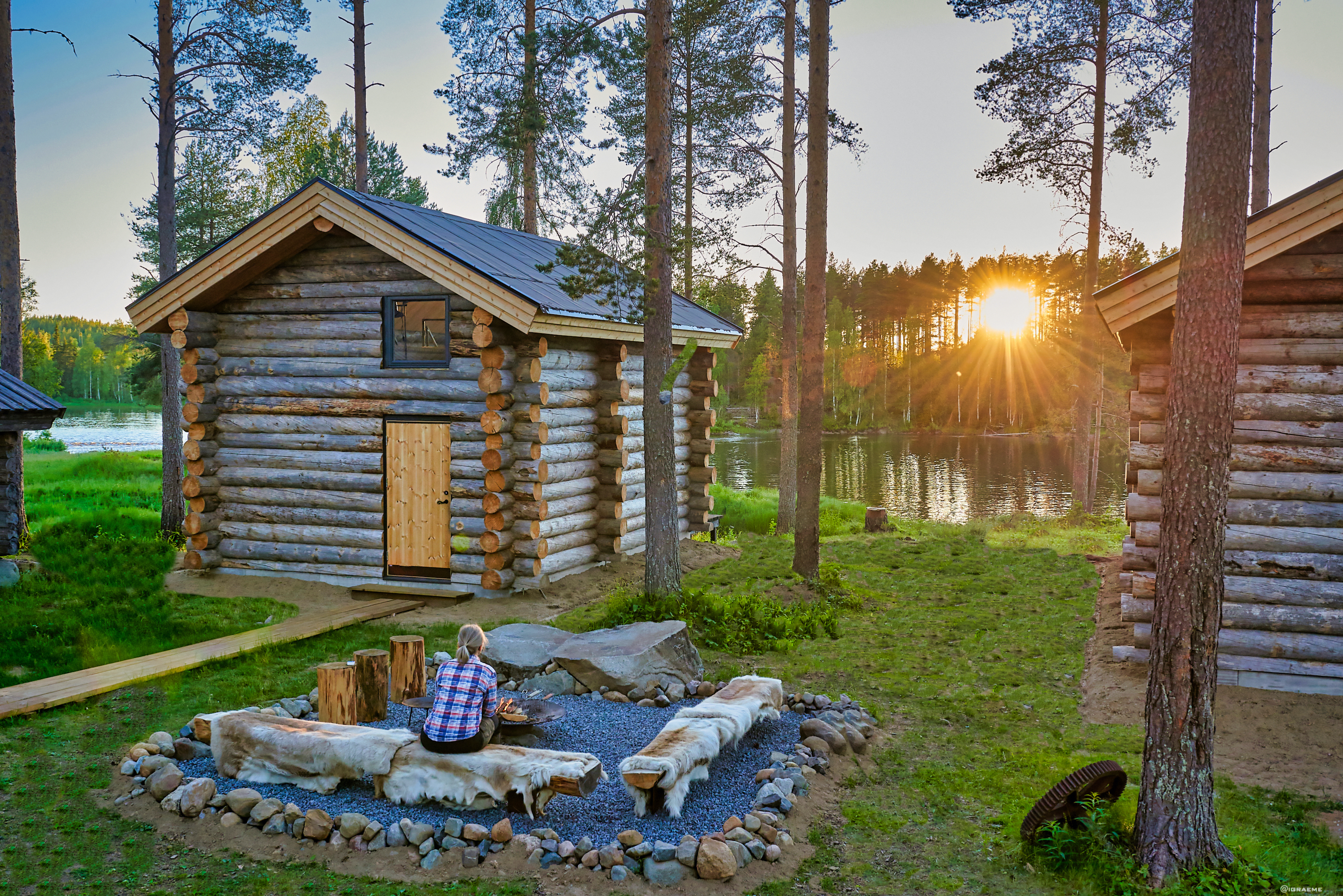 Arctic Retreat cabin exteriors and communal firepit overlooking river, sun setting amongst tall trees