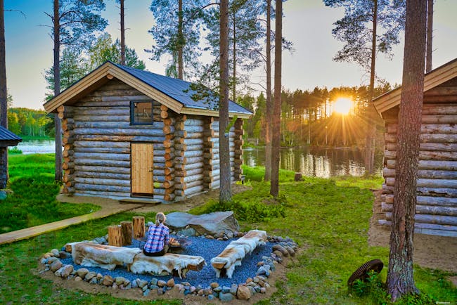 Arctic Retreat cabin exteriors and communal firepit overlooking river, sun setting amongst tall trees