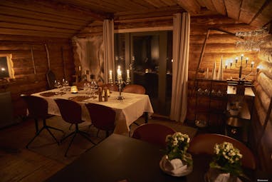 Arctic Retreat dining cabin, cosy lighting, timber walls, table set with candlesticks