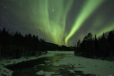Arctic Retreat northern lights over icy river and woodland