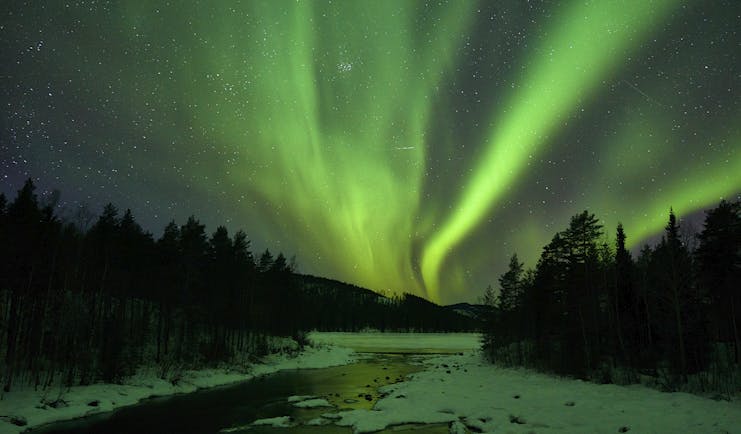 Arctic Retreat northern lights over icy river and woodland