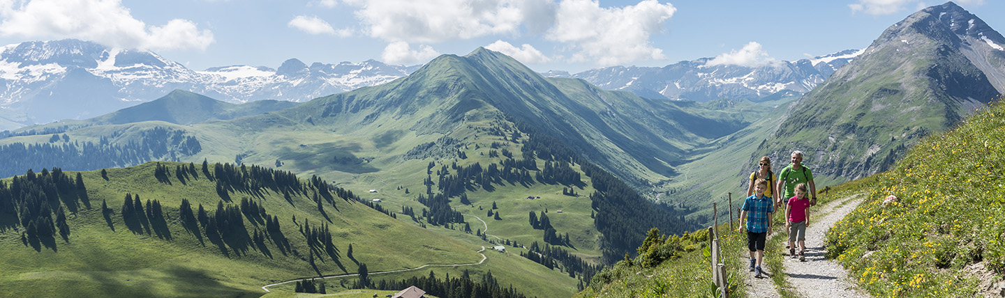 Family on mountain track walking with panorama of mountains behind