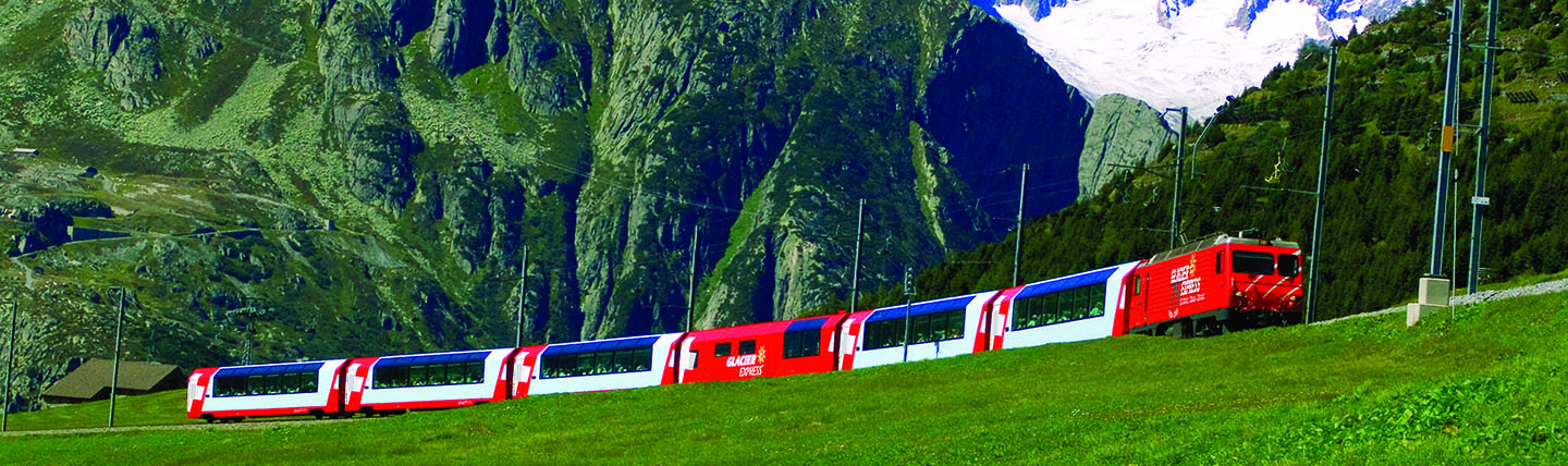 Red and white train in distance in front of wall of mountains