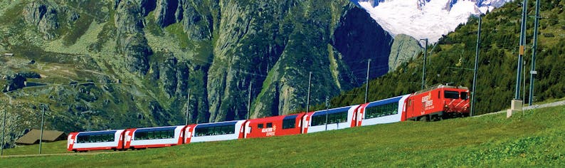 Red and white train in distance in front of wall of mountains