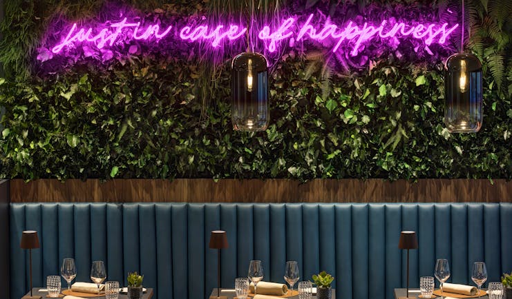 Hotel Lugano Dante bar, tables with drinks and napkins, bench seating, green leafy wall installation