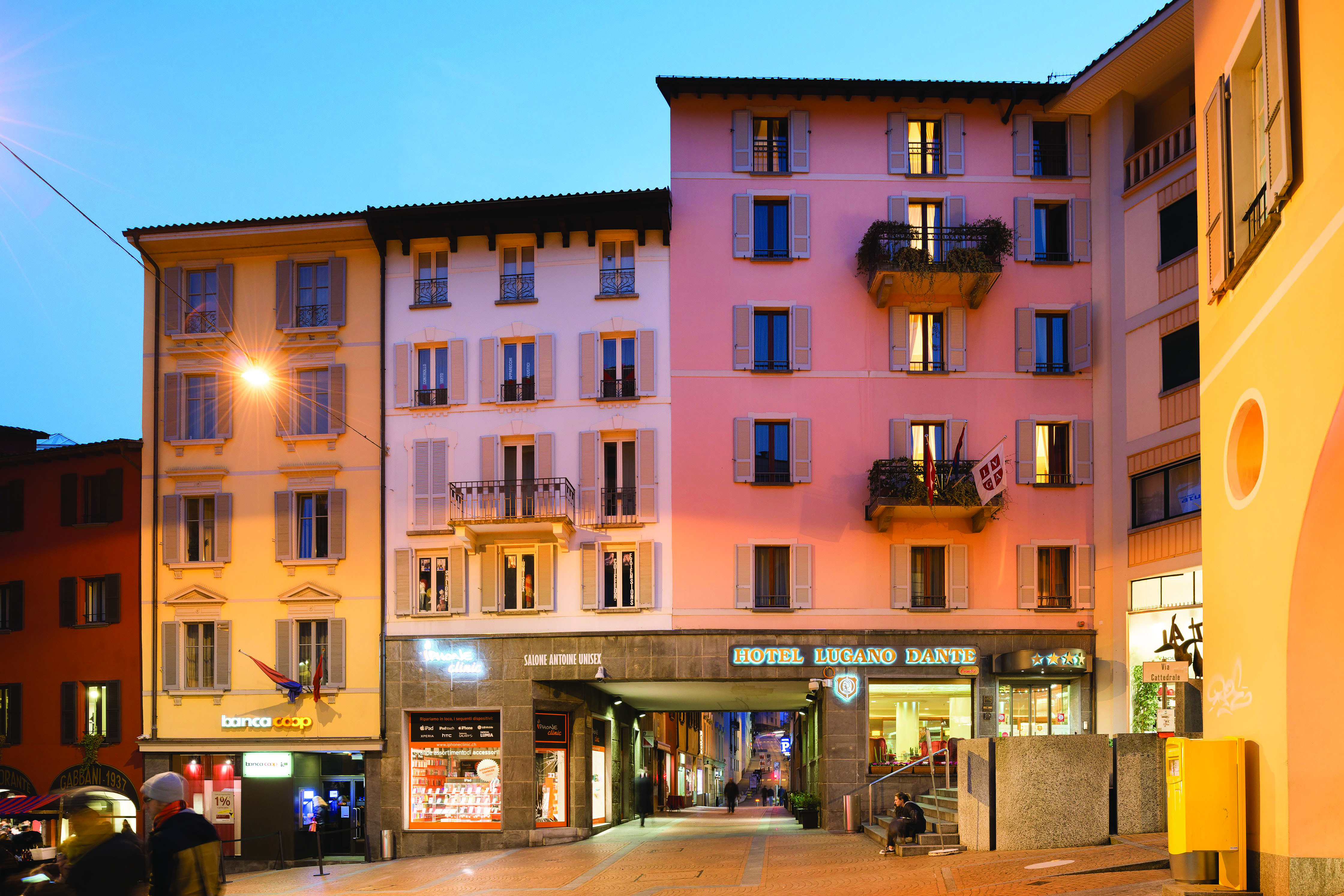Hotel Lugano Dante exterior, pink hotel building, shop fronts, sunset, town square