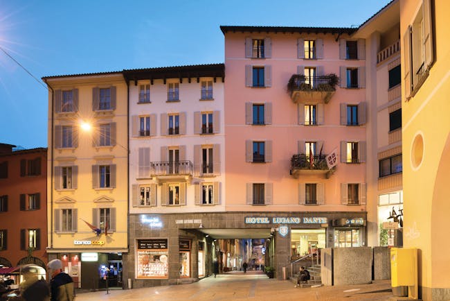 Hotel Lugano Dante exterior, pink hotel building, shop fronts, sunset, town square