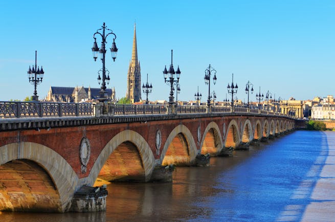 Bridge with lamps and spire of cathedral in distance in Bordeaux